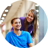 Smiling man in a wheelchair with a woman standing behind him, both looking happy in a shopping mall