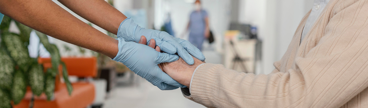 Healthcare worker wearing gloves holding hands with an elderly patient