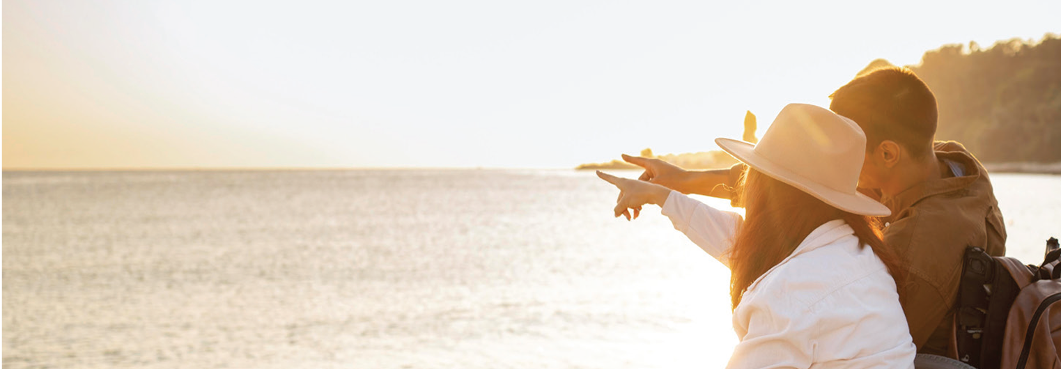 Couple sitting by the water at sunset, pointing toward the horizon