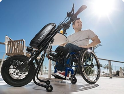 Man in a wheelchair with an electric handbike attachment outdoors on a sunny day