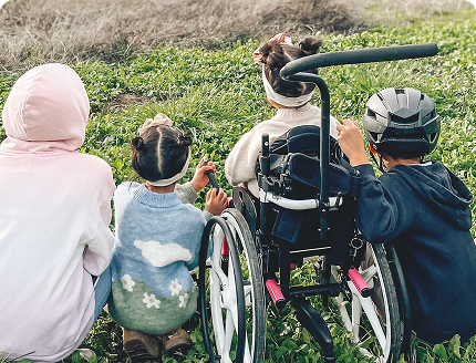 Four children sitting in a grassy field, including one using a wheelchair, enjoying nature together.