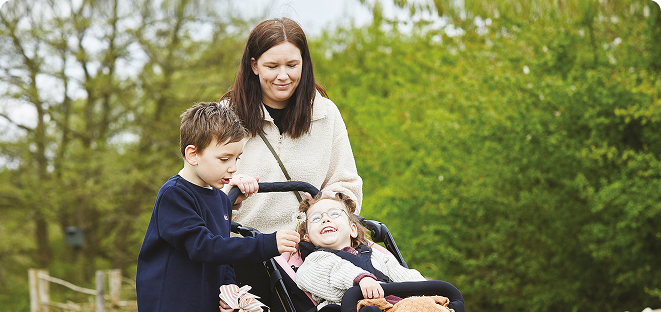 Woman with two children outdoors, smiling at a young girl sitting in a wheelchair stroller