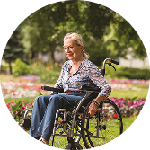 Smiling older woman sitting in a wheelchair outdoors in a flower-filled park